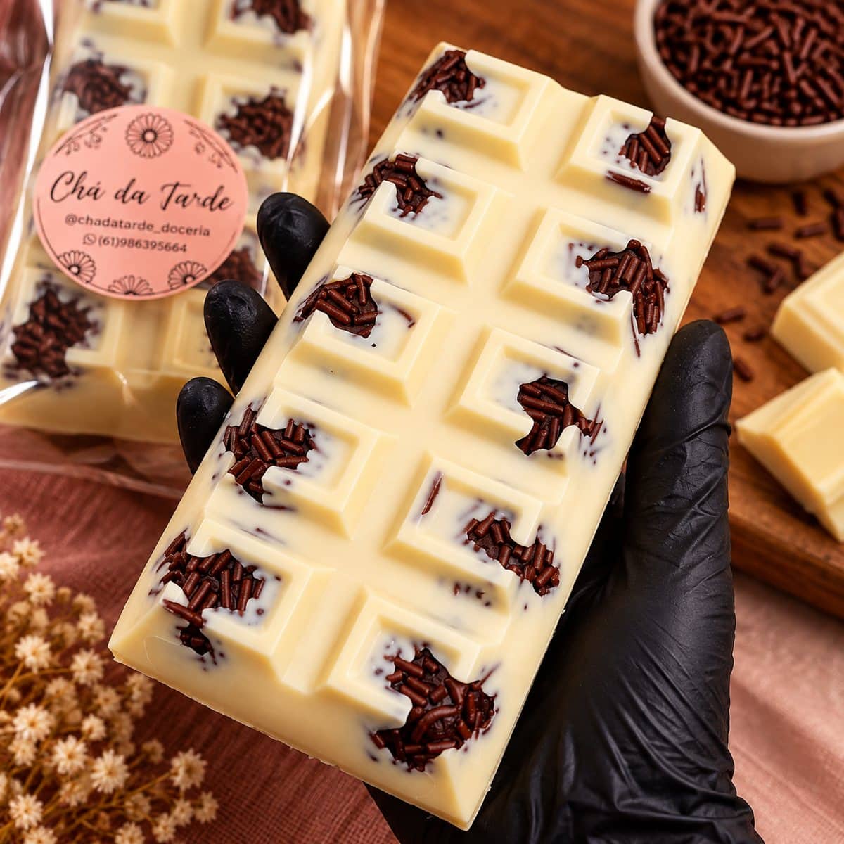 Barra de chocolate branco com granulado e recheio aparente, sobre tecido em tom terracota